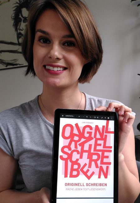 Julia posiert mit einem Tablet, auf dem die Titelseite ihres E-Books zu sehen ist